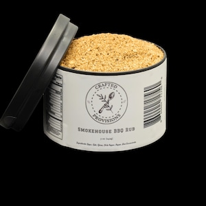 Puede incluir: Un tarro blanco con tapa negra lleno de una mezcla de especias marrones. La etiqueta dice "Crafted Provisions Smokehouse BBQ Rub".