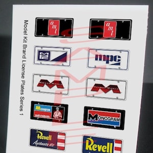 May include: A set of ten model kit brand license plates, featuring various logos and names, including MPC, Monogram, Revell, and Authentic Kit. The plates are printed on white paper with a black border.