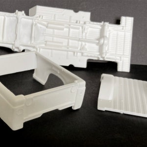 May include: White plastic model car parts for a pickup truck. The parts include the bed, chassis, and floor.