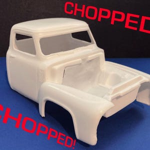 May include: A white, unpainted model of a classic pickup truck cab and bed. The word "CHOPPED!" is written in red diagonally across the image. The model is on a blue surface with a black background.
