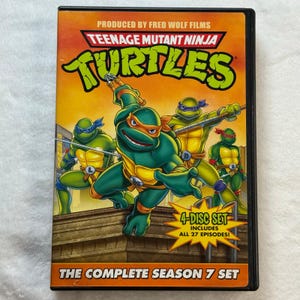 May include: Teenage Mutant Ninja Turtles Season 7 DVD set. The cover features the four turtles in action poses, with the title in large, green, stylized letters. The DVD case is a 4-disc set that includes all 27 episodes.