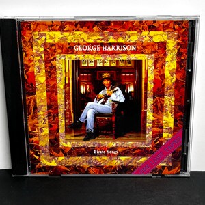 May include: CD case featuring George Harrison's album "Pirate Songs." The cover art showcases a portrait of Harrison playing an instrument, set within a series of ornate, colorful frames. The text "George Harrison" and "Pirate Songs" are visible.