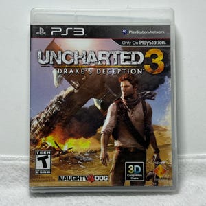 May include: A PlayStation 3 video game case for Uncharted 3: Drake's Deception. The cover art features a man in a desert setting with a crashed airplane in the background, the ESRB Teen rating, and a 3D compatible game logo on the front.