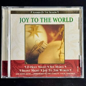 May include: A music CD titled Sounds of the Season Joy to the World. The cover features a gold ornament and star graphic. Track titles include O Holy Night, Ave Maria, Silent Night, and Joy to the World, performed by the Starlite Vocal Ensemble.