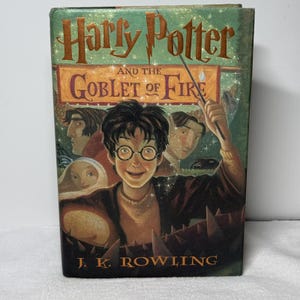 May include: A hardcover book titled Harry Potter and the Goblet of Fire by J.K. Rowling. The green cover features an illustration of a young person with round glasses holding a wand, surrounded by other characters and a glowing light effect.