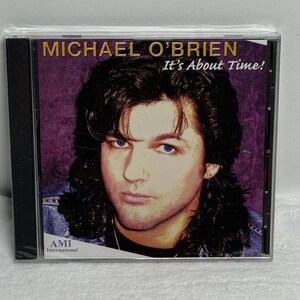 May include: A music CD case featuring the album cover for Michael O'Brien titled It's About Time! The cover displays a portrait of a person with dark, shoulder-length hair and blue eyes against a purple background, with the AMI International logo.