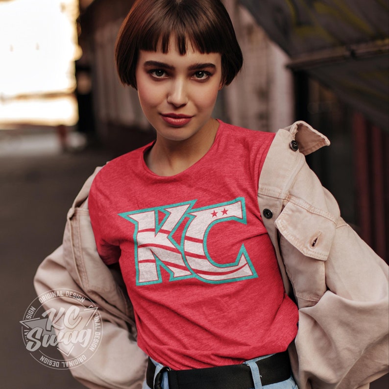KC Swag - Kansas City Current, Flowing KC on Heather red unisex t-shirt worn by female model under an open jacket standing in front of an old barn