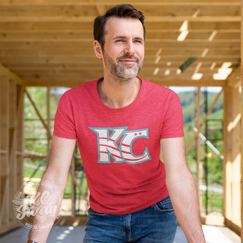 KC Swag - Kansas City Current, Flowing KC on Heather red unisex t-shirt worn by male model standing in a framed home construction zone