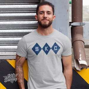 Kansas City Soccer T-shirt, Sporting-Inspired Argyle Diamonds Club Athletic Heather Gray Tee worn by male model leaning on a loading dock in an urban setting