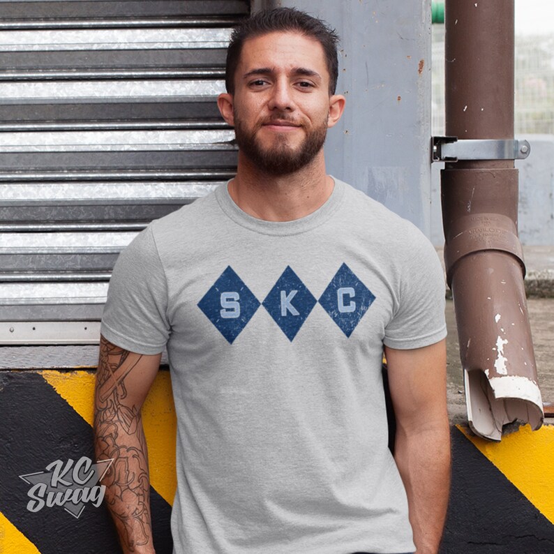 Kansas City Soccer T-shirt, Sporting-Inspired Argyle Diamonds Club Athletic Heather Gray Tee worn by male model leaning on a loading dock in an urban setting