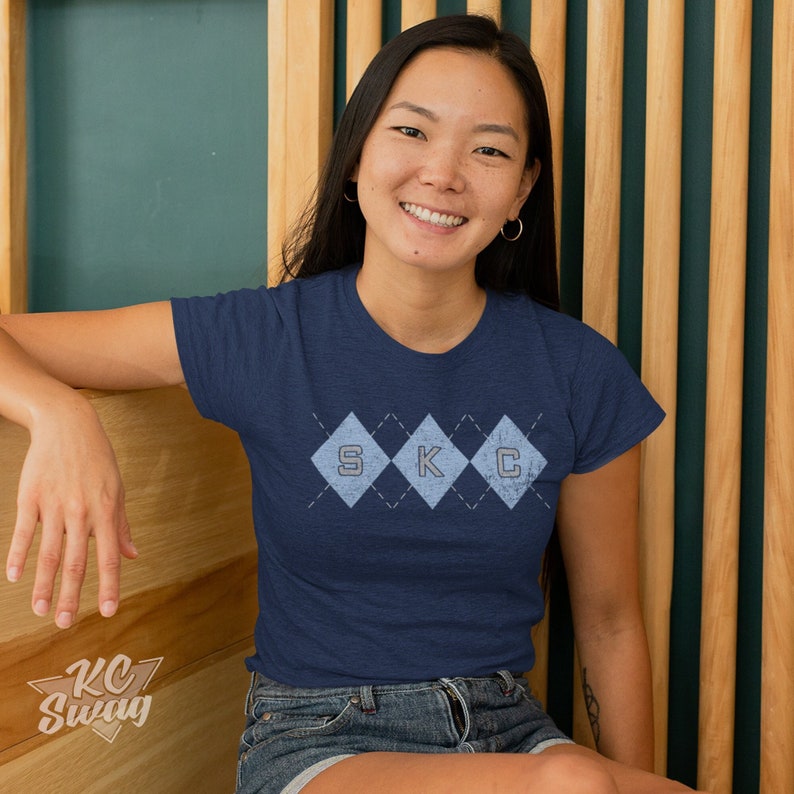 Kansas City Soccer T-shirt, Sporting-Inspired Argyle Diamonds Club Heather Navy Tee worn by female model sitting on a wood bench in front of a wood-slatted wall