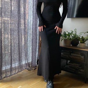 K&ouml;nnte beinhalten: Ein schwarzes, schulterfreies Maxikleid mit langen &Auml;rmeln und einer figurbetonten Silhouette. Das Kleid hat einen leichten Ausbruch am Saum.