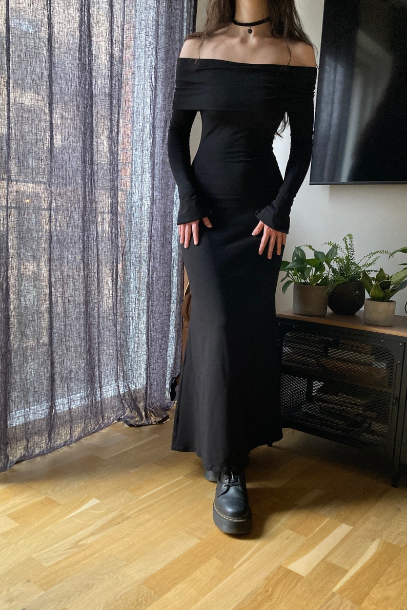 K&ouml;nnte beinhalten: Ein schwarzes, schulterfreies Maxikleid mit langen &Auml;rmeln und einer figurbetonten Silhouette. Das Kleid hat einen leichten Ausbruch am Saum.