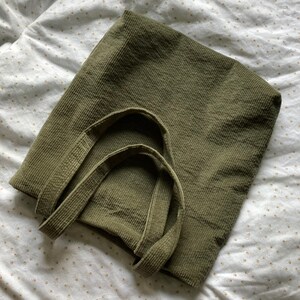 May include: A green corduroy tote bag with two handles. The bag is made of a soft, textured fabric.