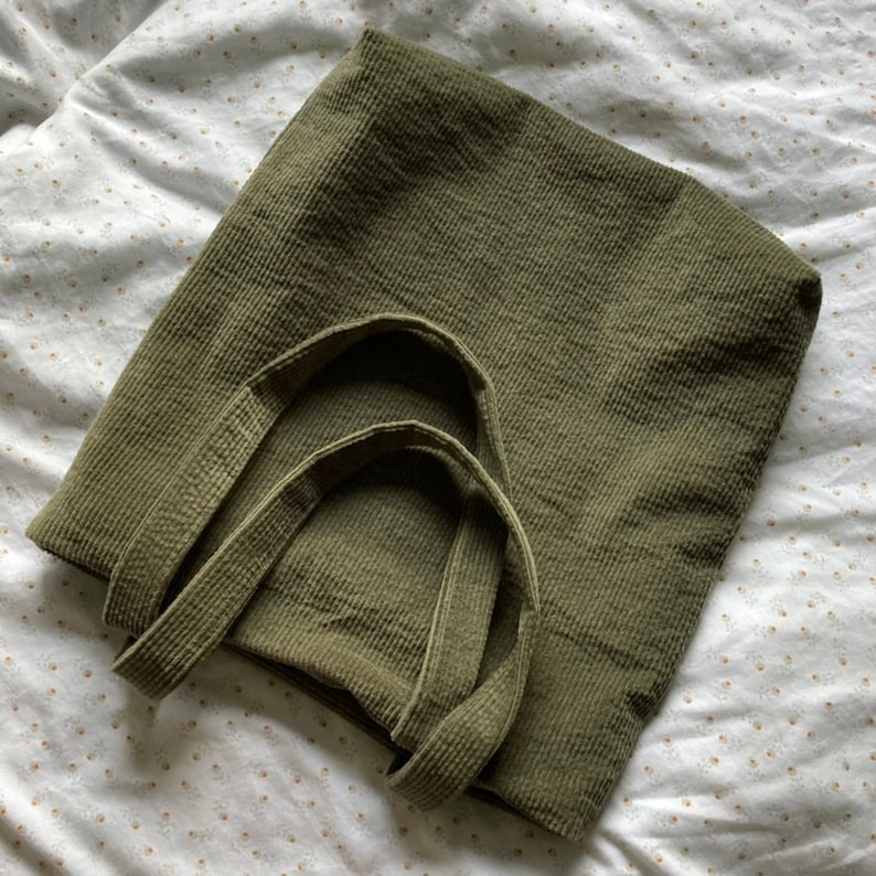 May include: A green corduroy tote bag with two handles. The bag is made of a soft, textured fabric.
