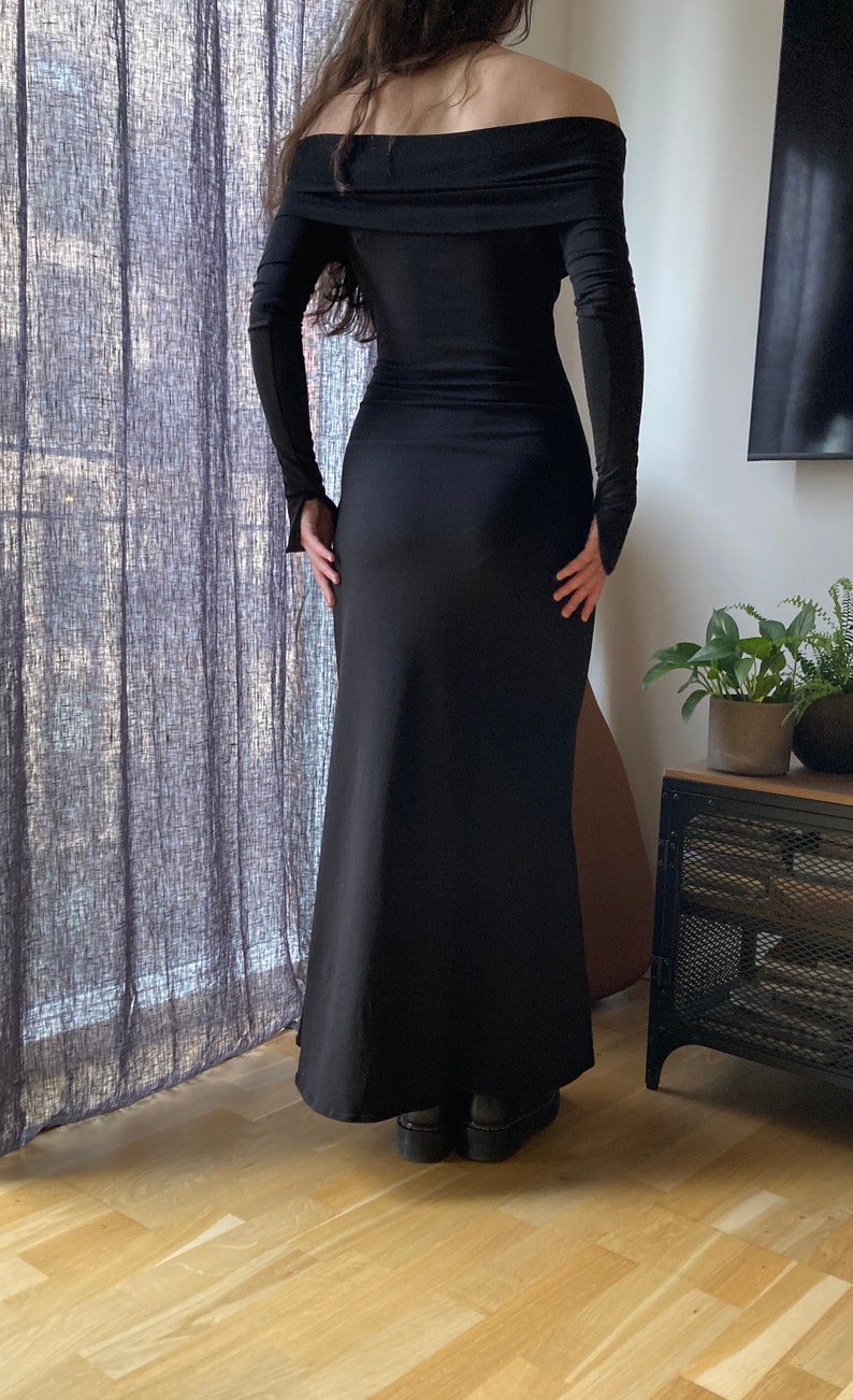 K&ouml;nnte beinhalten: Ein langes schwarzes Maxikleid mit offener Schulter und langen &Auml;rmeln. Das Kleid ist am Oberteil figurbetont und geht in einen weiten Rock &uuml;ber.