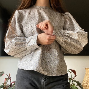 May include: A white blouse with a floral pattern and puffed sleeves. The blouse has a round neckline and is made of a lightweight fabric.