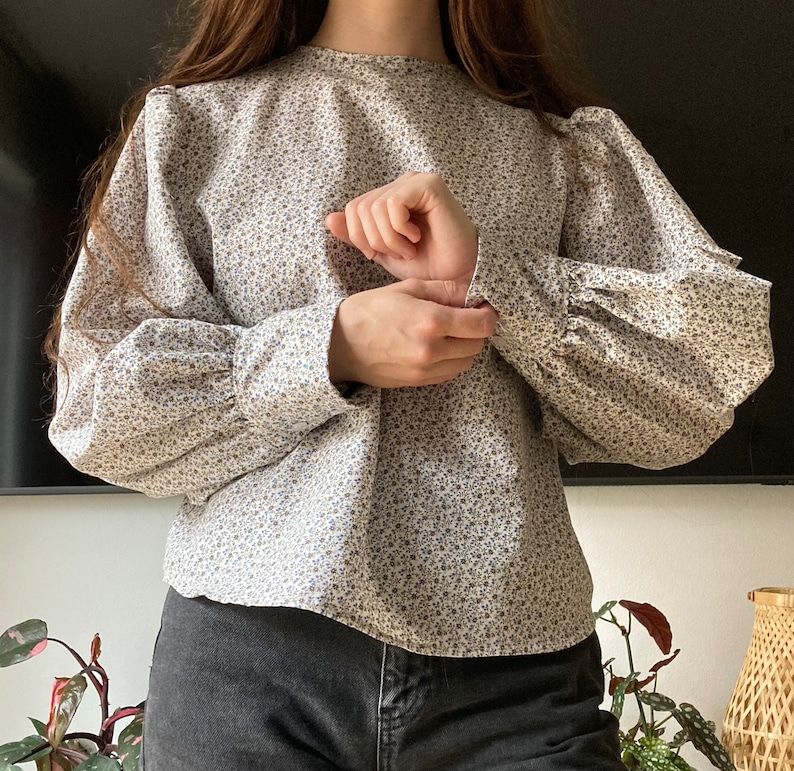 May include: A white blouse with a floral pattern and puffed sleeves. The blouse has a round neckline and is made of a lightweight fabric.