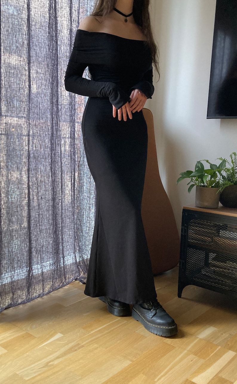 K&ouml;nnte beinhalten: Ein schwarzes, schulterfreies Maxikleid mit langen &Auml;rmeln. Das Kleid hat einen figurbetonten Oberteil und einen flie&szlig;enden Rock.