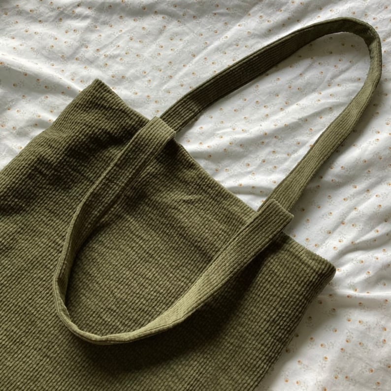 May include: A green corduroy tote bag with two long straps. The bag is made of a soft, textured fabric.