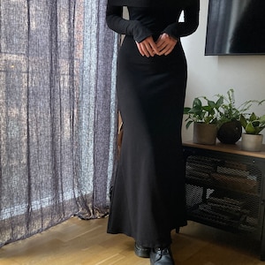K&ouml;nnte beinhalten: Ein schwarzes, schulterfreies Maxikleid mit langen &Auml;rmeln. Das Kleid hat einen figurbetonten Oberteil und einen flie&szlig;enden Rock.