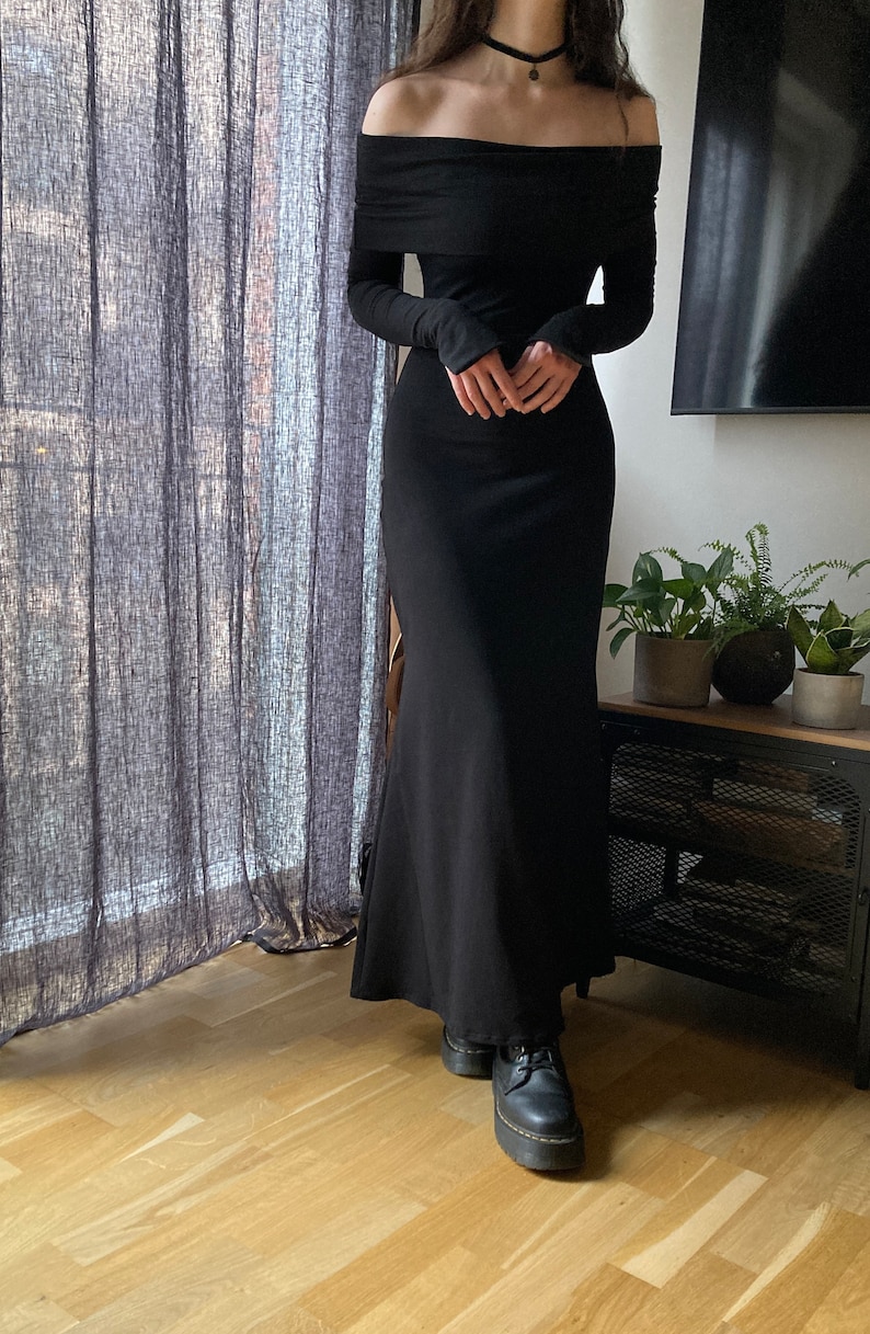 K&ouml;nnte beinhalten: Ein schwarzes, schulterfreies Maxikleid mit langen &Auml;rmeln. Das Kleid hat einen figurbetonten Oberteil und einen flie&szlig;enden Rock.
