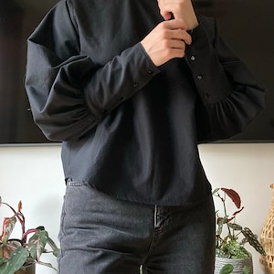 May include: A black mock neck shirt with long sleeves and buttoned cuffs. The shirt has a slightly puffed sleeve. The shirt is paired with dark wash jeans.
