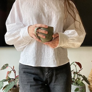 May include: A white, eyelet-embellished blouse with long, puffed sleeves. The blouse is worn with black jeans.