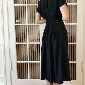May include: A black midi dress with short sleeves and a gathered back. The dress is knee-length and has a relaxed fit.