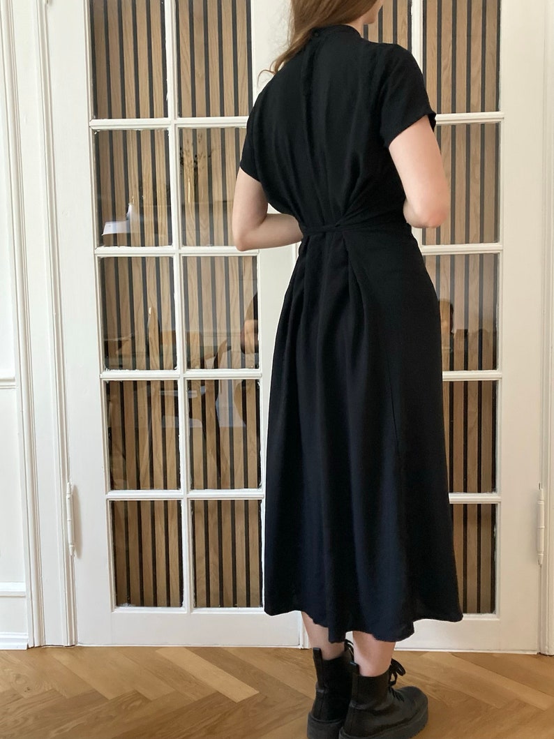 May include: A black midi dress with short sleeves and a gathered back. The dress is knee-length and has a relaxed fit.