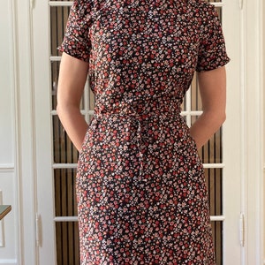 May include: A black midi dress with a high neck and short sleeves. The dress is covered in a small floral print with red, white, and pink flowers.