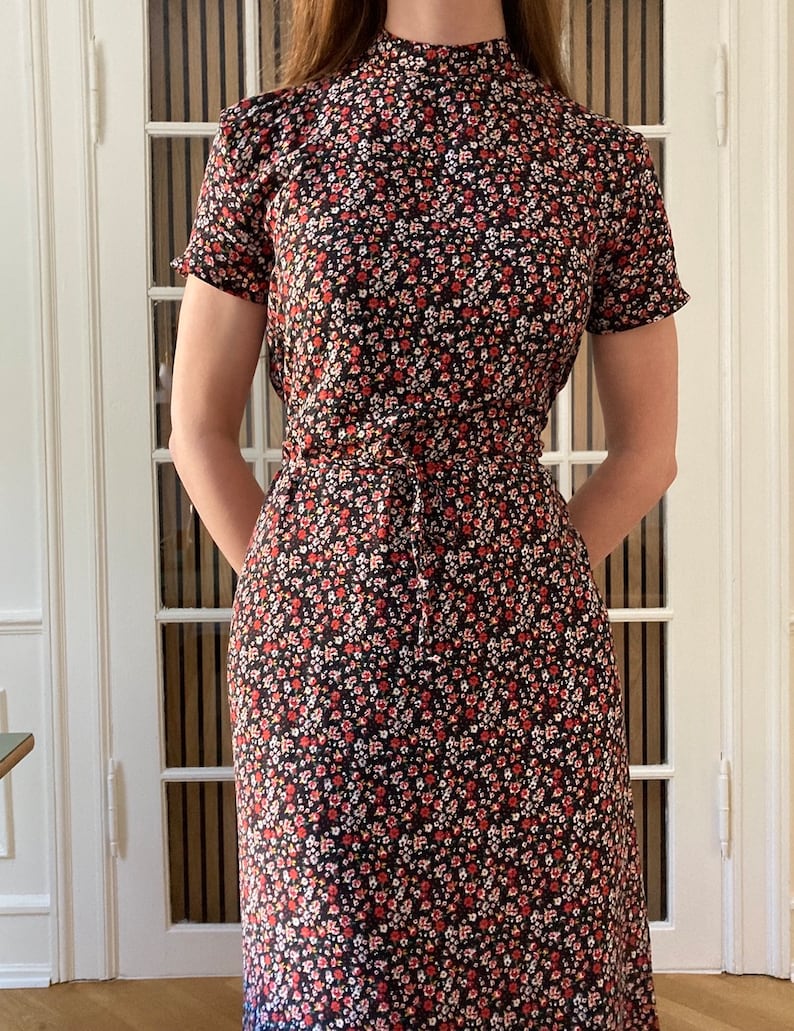 May include: A black midi dress with a high neck and short sleeves. The dress is covered in a small floral print with red, white, and pink flowers.