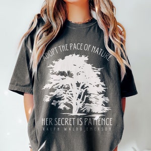 May include: A dark grey t-shirt with a white tree graphic and the text "Adopt the pace of nature. Her secret is patience. Ralph Waldo Emerson".
