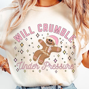 May include: A white t-shirt with a pink and brown gingerbread man graphic and the text "WILL CRUMBLE Under Pressure".