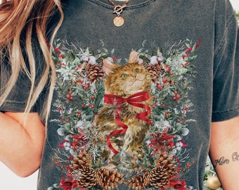May include: A gray t-shirt with a Christmas-themed design featuring a cat wearing a red bow and surrounded by pine cones, holly, and berries.