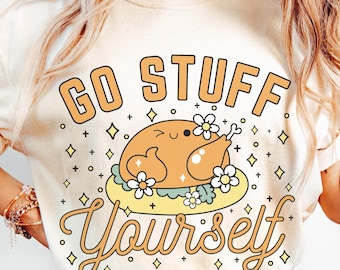 Può includere: Una maglietta bianca con un disegno di un tacchino dei cartoni animati con il testo "Go Stuff Yourself" in lettere arancioni e gialle.