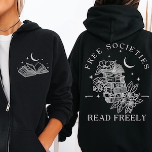 May include: Black zip-up hoodie with a white graphic of an open book and crescent moon on the front. The back features the text "FREE SOCIETIES READ FREELY" with a stack of books, flowers, and a crescent moon design. A casual, comfortable garment.