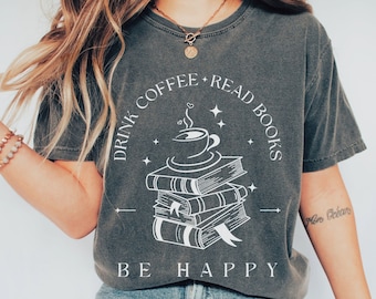 May include: A dark gray t-shirt with a white graphic design of a stack of books with a coffee cup on top. The text on the shirt reads "Drink Coffee + Read Books" and "Be Happy".