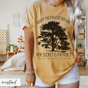 May include: A mustard yellow t-shirt with a black silhouette of a tree and the text "Adopt the pace of nature. Her secret is patience. Ralph Waldo Emerson."
