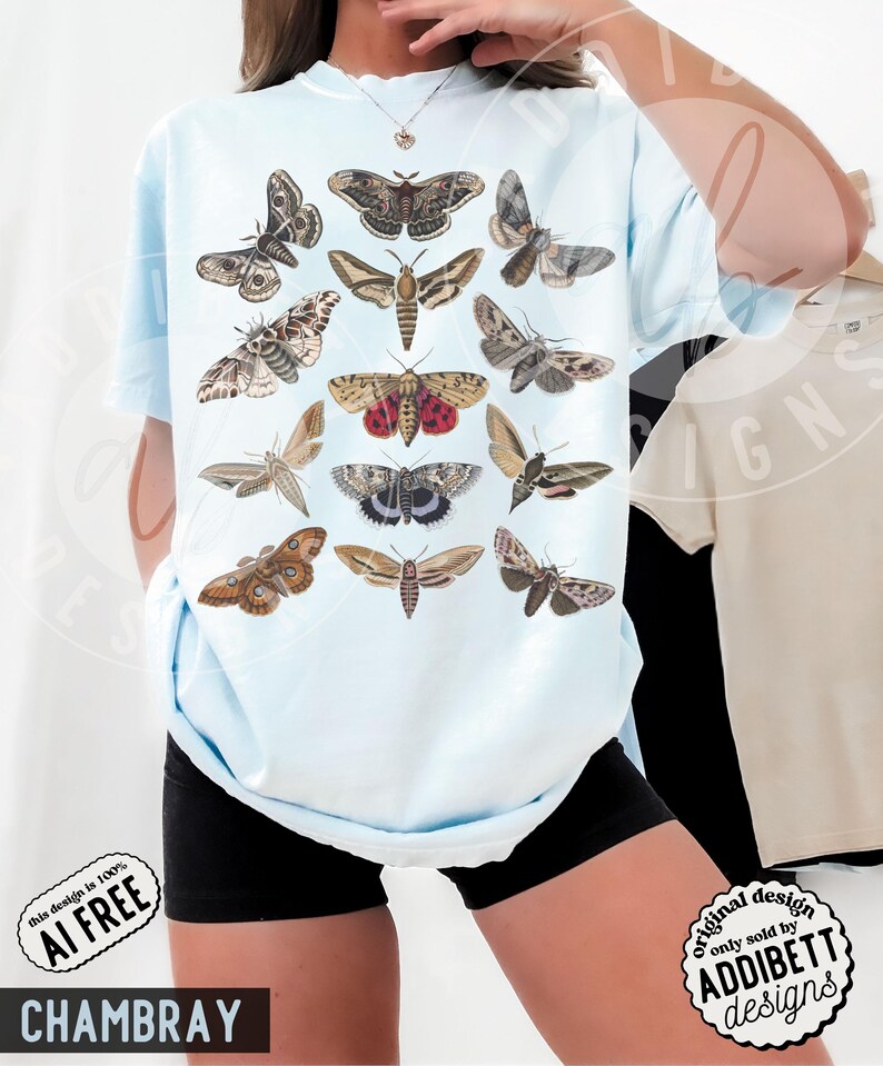 May include: A light blue t-shirt featuring a graphic print of twelve different moth species arranged in a grid. The moths are depicted in various shades of brown, tan, grey, and red, showcasing intricate wing patterns and detailed anatomical features.