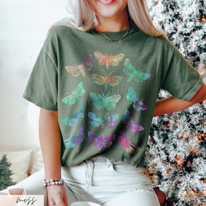 May include: A green t-shirt featuring a colourful moth design. The moths are arranged in a circular pattern and have iridescent wings.