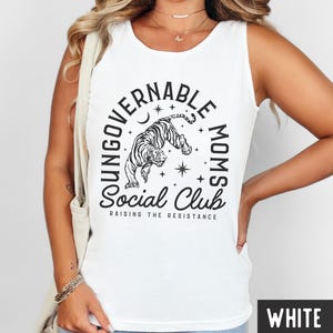 Puede incluir: Camiseta sin mangas blanca con un gr&aacute;fico en blanco y negro. El gr&aacute;fico presenta un tigre, estrellas y las palabras "UNGOVERNABLE MOMS Social Club" y "RAISING THE RESISTANCE". La camiseta sin mangas es sin mangas.