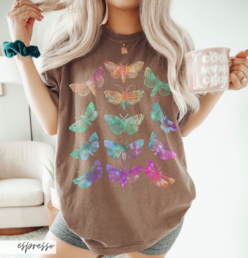 May include: An oversized brown t-shirt featuring a colourful butterfly graphic print. The butterflies are arranged in a pattern and are iridescent.