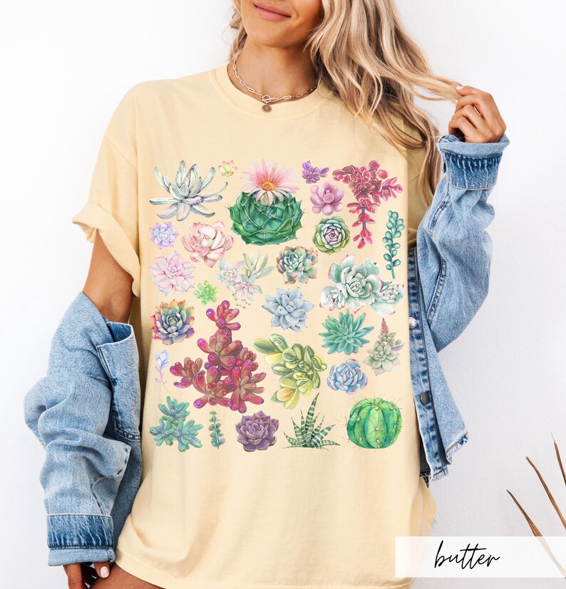 Puede incluir: Una camiseta amarilla con un estampado acuarela colorido de diferentes suculentas. El estampado presenta una variedad de formas, tama&ntilde;os y colores de suculentas.