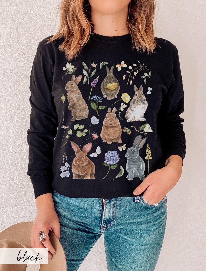 May include: Black long-sleeved shirt with a graphic print of multiple rabbits and flowers. The rabbits are brown, gray, and white.