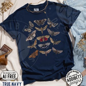 May include: A dark navy blue short-sleeve t-shirt featuring a central graphic print of various moth species in shades of brown, tan, grey, and red. The design displays multiple moth illustrations arranged in a cluster on the front of the garment.