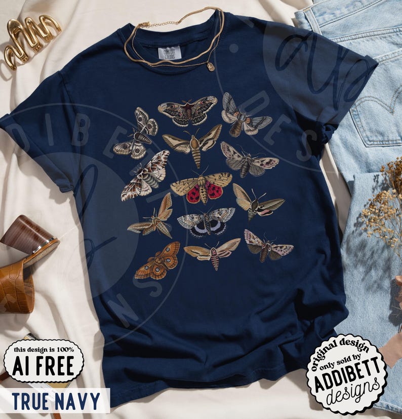 May include: A dark navy blue short-sleeve t-shirt featuring a central graphic print of various moth species in shades of brown, tan, grey, and red. The design displays multiple moth illustrations arranged in a cluster on the front of the garment.