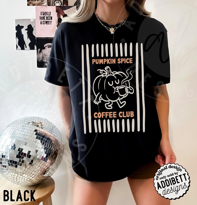 May include: A black short-sleeve t-shirt featuring a white graphic of a cartoon pumpkin drinking from a mug. The text PUMPKIN SPICE COFFEE CLUB is printed in orange above and below the pumpkin, framed by vertical white lines on both sides.