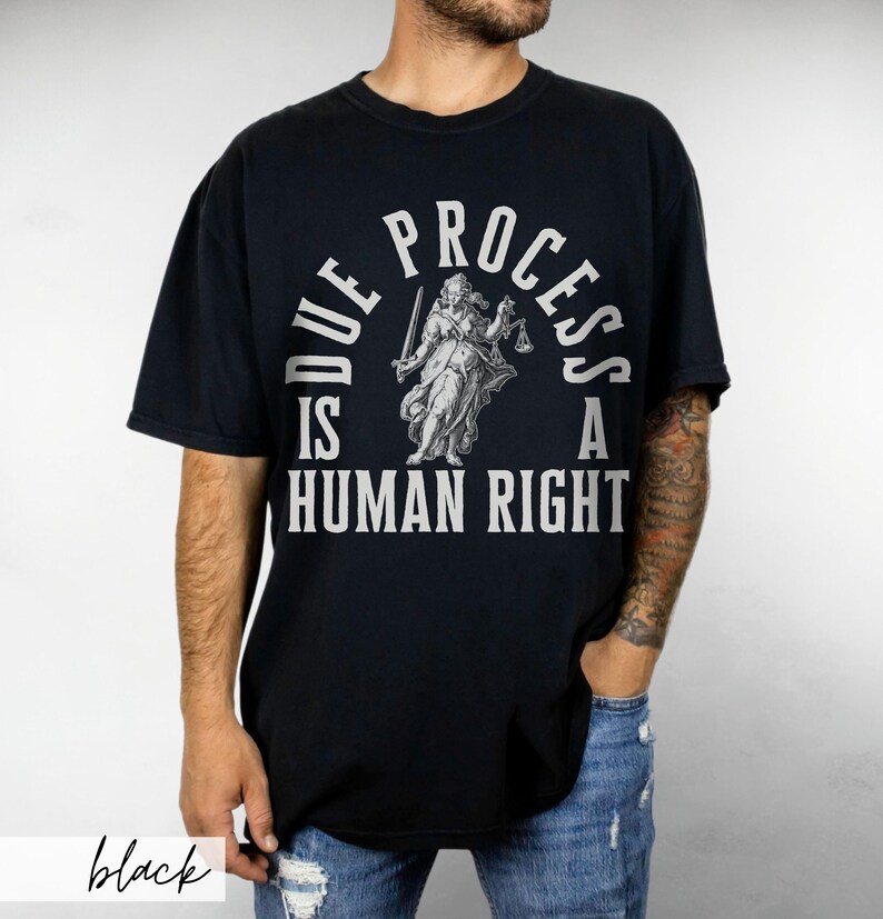 May include: Black t-shirt with a white graphic print of a woman holding scales of justice. The text reads "Due Process Is A Human Right".
