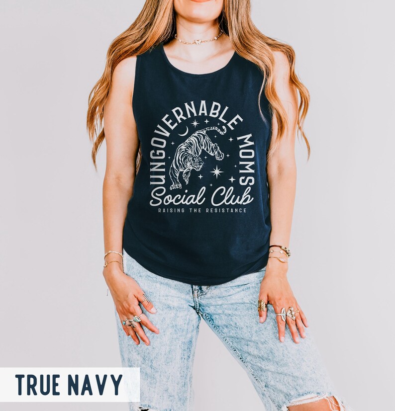 Puede incluir: Camiseta sin mangas azul marino con el texto "UNGOVERNABLE MOMS Social Club" y un gr&aacute;fico de tigre. El texto "RAISING THE RESISTANCE" est&aacute; debajo. La camiseta sin mangas es sin mangas y de material suave.